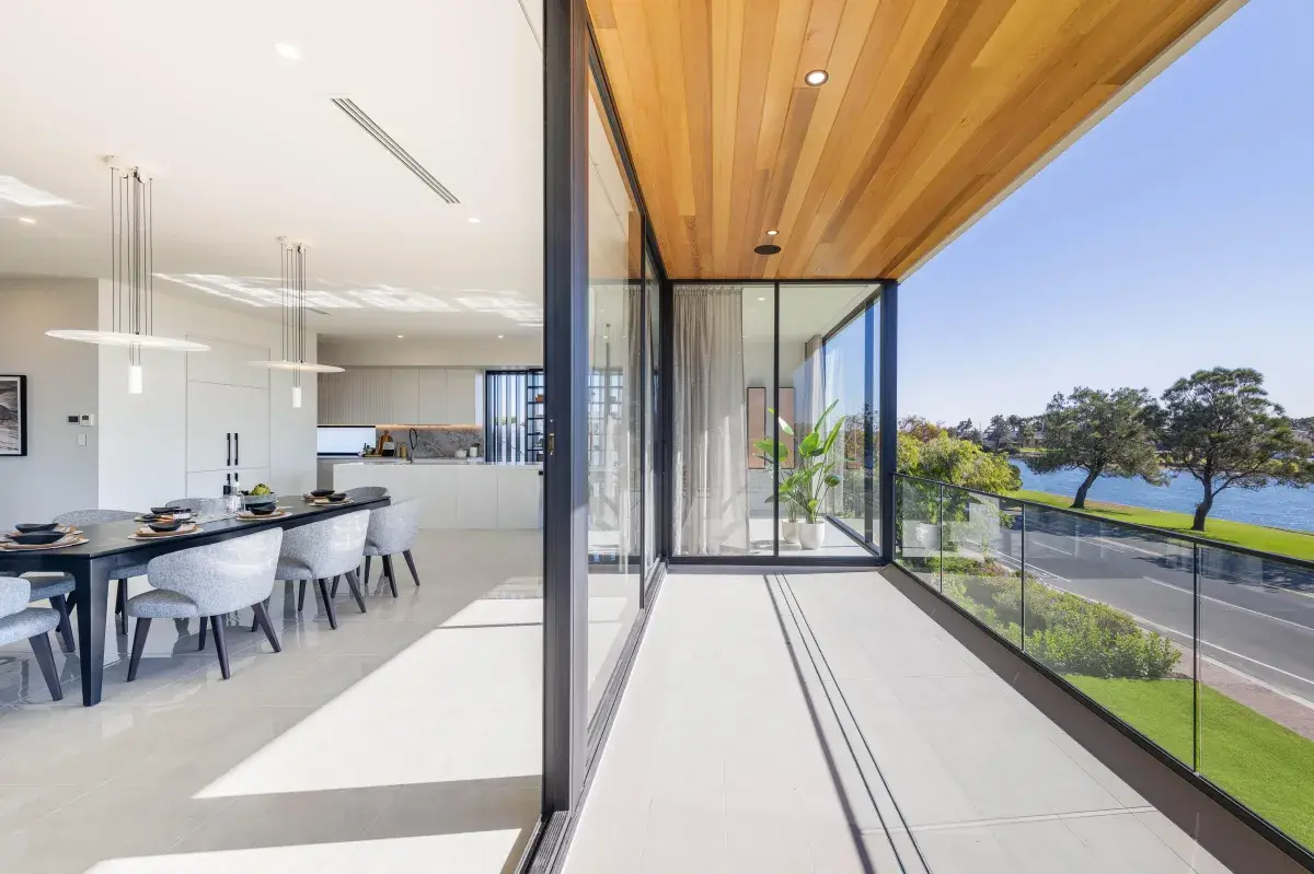 Black aluminium sliding doors opening a modern dining area onto a waterside balcony